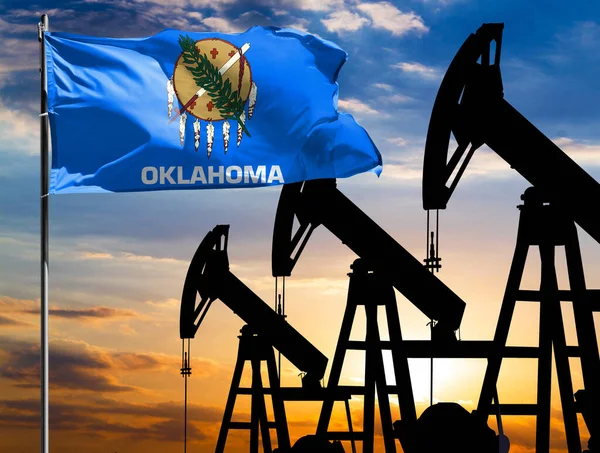 Oil rigs against the backdrop of the colorful sky and a flagpole with the flag State of Oklahoma. The concept of oil production, minerals, development of new deposits.