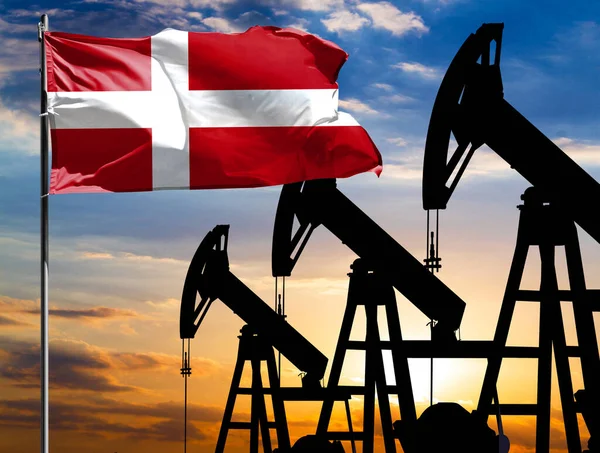 Oil rigs against the backdrop of the colorful sky and a flagpole with the flag of Denmark. The concept of oil production, minerals, development of new deposits.