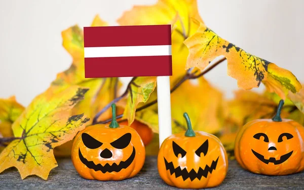 Colorful Halloween background with smiley pumpkins and toy flag of Latvia