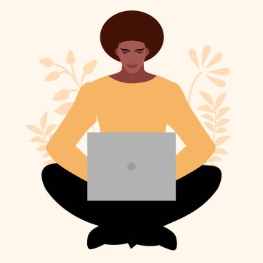 Afrikalı genç bir adam dizüstü bilgisayarla rahatça oturuyor, bitkilerle çevrili. 