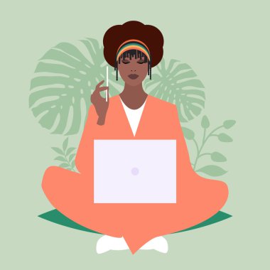 Afrikalı iş kadını dizüstü bilgisayar ve kalemle rahatça oturuyor, bitkilerle çevrili. 