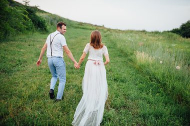 Mutlu gelin ve damat yeşil çimenlerin üzerinde yürüyüş