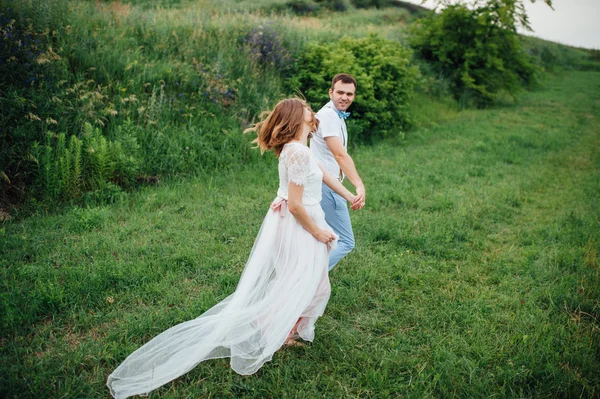 Счастливой невесты и жениха, идущих по зеленой траве — стоковое фото