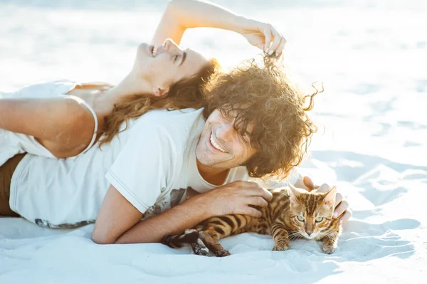 Alegre jovem casal se divertindo na praia com seu gato bengala — Fotografia de Stock