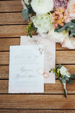 Yeni evli konuklar için düğün davetiyesi. Yüzükler ve gelin buketi yan yana yatıyor.