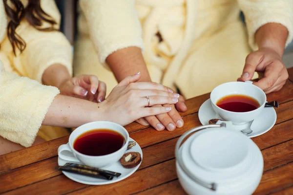 A loving couple sits in dressing gowns and drinks tea on a wooden table — Stock Photo, Image