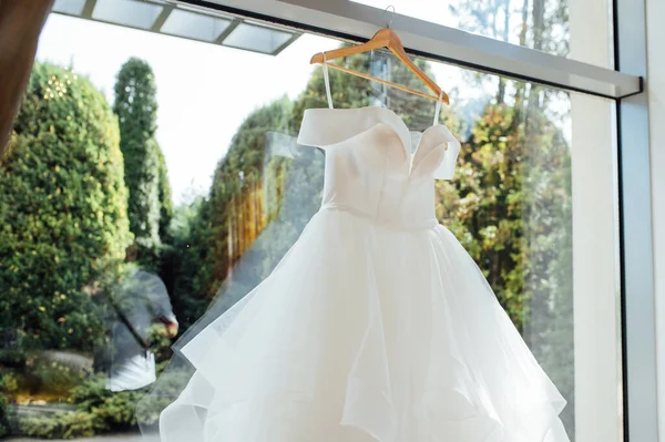 Robe de mariée blanche suspendue à un poteau rideau avec le soleil qui brille à travers la fenêtre — Photo