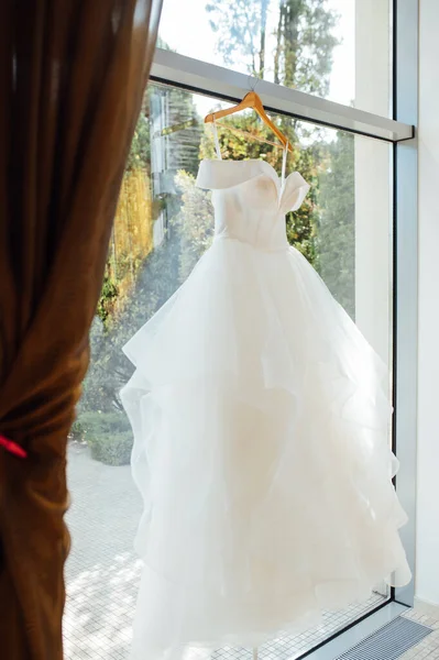 white Wedding dress hanging from a curtain pole with the sun shining through the window