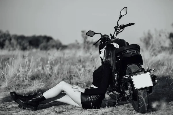 Menina bonita em roupas pretas senta-se na motocicleta e posa para câmera. Pôr-do-sol — Fotografia de Stock