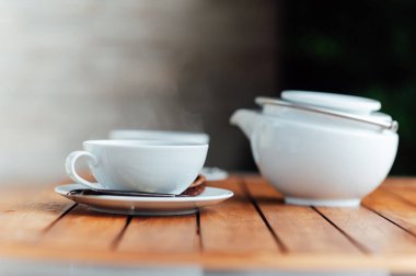 Beyaz sofra takımı, büyük çaydanlık, fincan, kase, gri bir arka planda porselen kaşık.