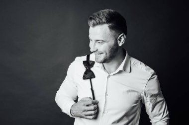 Beyaz gömlekli yakışıklı adam omzunda papyon tutuyor.