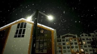 Geceleri şehirdeki bir apartmanın arka planına kar yağıyor.