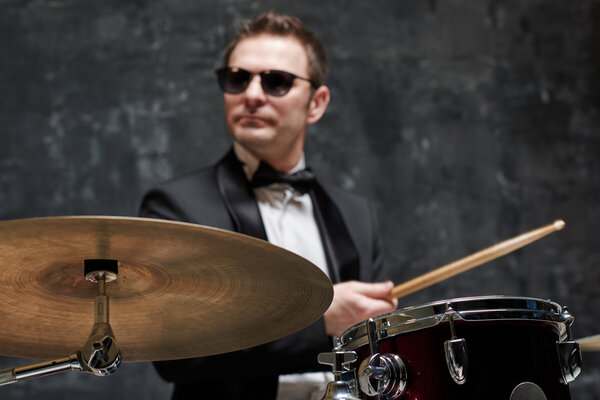 Blurred handsome man in sunglasses and suit playing a drum