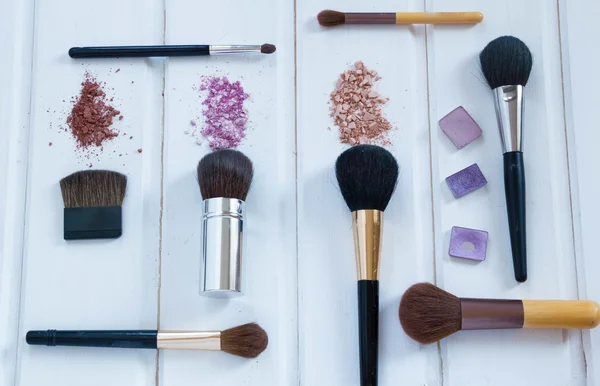 Accesorios cosméticos de las mujeres. Pinceles de maquillaje y sombra de ojos aplastada sobre fondo de madera —  Fotos de Stock