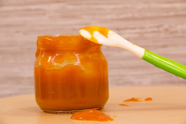 Baby food puree carrots in a glass bottle with a spoon on the table amid. Selective focus. — Stock Photo, Image