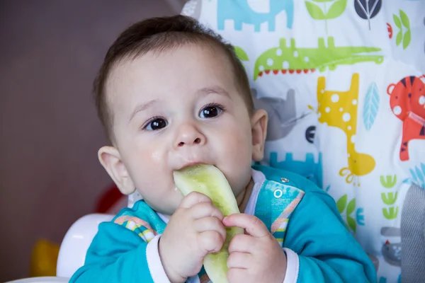 Bebê comendo legumes. numa cadeira alta. Um bebé a nascer, a comer o pepino, o conceito de comida de bebé, a alimentar o bebé. Lar recém-nascido. comida saudável. A primeira comida que uma criança come lanches nutritivos . — Fotografia de Stock