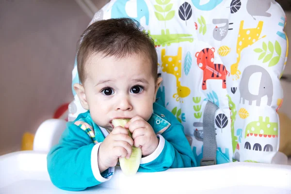 Bebê comendo legumes. numa cadeira alta. dentição, o pepino, o conceito de comida, alimentação. Lar recém-nascido. saudável. A primeira criança come lanches nutritivos . — Fotografia de Stock