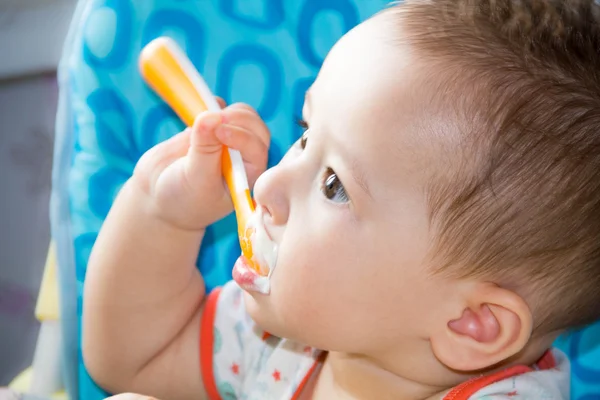 Pequeño niño feliz sentado en una silla y come yogur de cuya cara está manchado en la comida para bebés — Foto de Stock