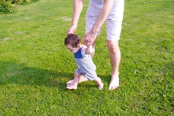 Pai e pernas de bebé. Fechar de como o pai sustenta o bebê quando ele dá os primeiros passos. mãos masculinas segurando as mãos do pequeno filho. conceito de família — Fotografia de Stock