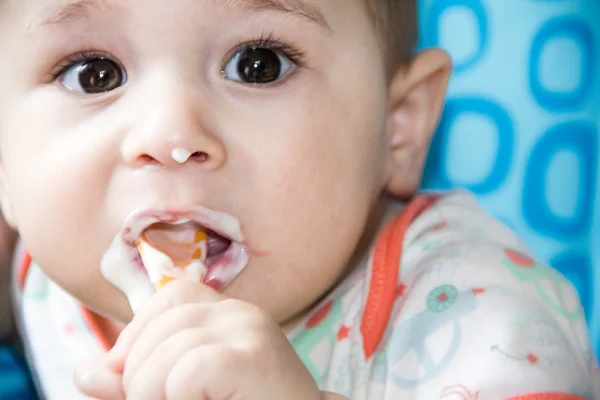 Small happy child sitting in a chair the concept of family, child health, feed the baby, eat at home. eats yogurt from whose face is marred in baby food. — Stock Photo, Image