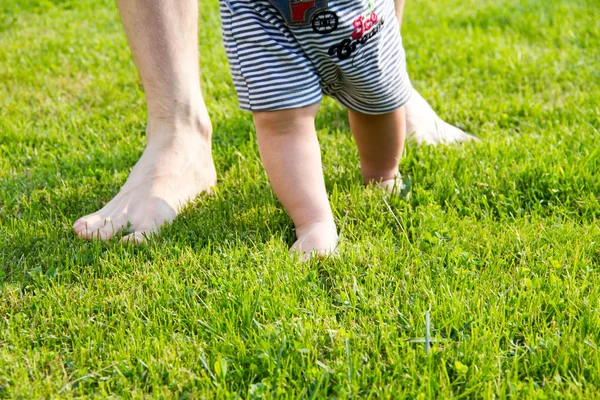 Apja és a baba lábát. Vértes hogyan az Atya támogatja a baba, amikor az első lépéseket teszi. férfi keze gazdaság kis fia kezét. a család fogalma — Stock Fotó