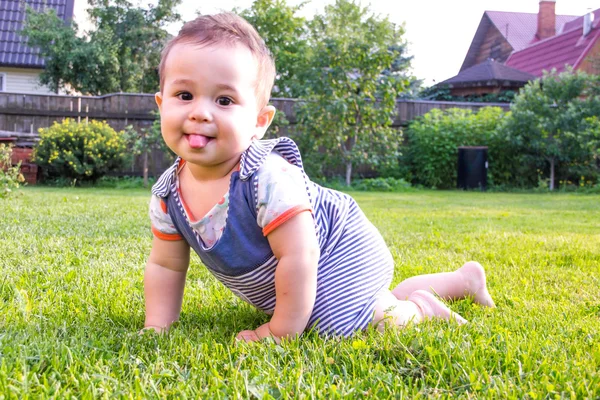 Lite baby lära sig krypa i gräset en solig sommardag. begreppet barns utveckling månader. glada barn som leker lekplats. rolig söt karaktär ansikte, kid fastnat visar tungan — Stockfoto