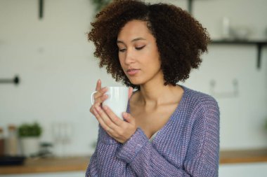 Mutfakta elinde bir fincan kahve tutan mutlu bir kadın. Genç Afro-Amerikan kadın kahve içiyor.