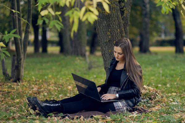 Jovem trabalha para um laptop no parque. o estudante está se preparando para exames — Fotografia de Stock