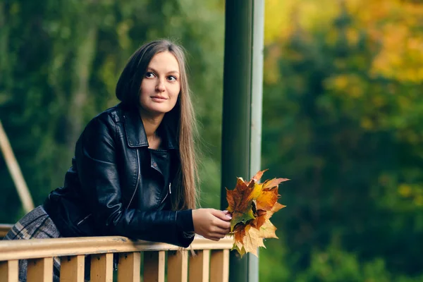 Mooie vrouw kijkt in de verte leunend op de reling. portret van een dame met esdoorn bladeren in haar handen — Stockfoto