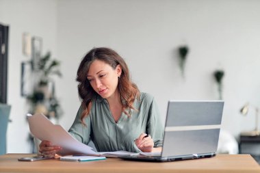 Merkez ofisten çalışan genç bir kadın. Bilgisayarı ve interneti kullanan serbest çalışan. Oturma odasındaki işyeri.