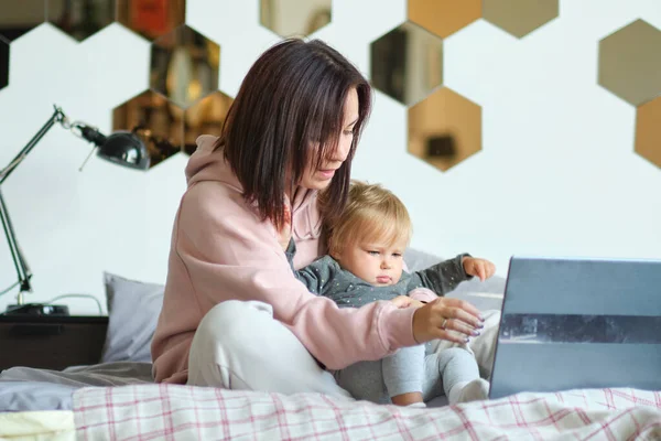 Anya távolról dolgozik a laptopon, miközben vigyáz a babájára. Fiatal anya szülési szabadságon próbál szabadúszó lenni az asztalnál egy kisgyerekkel. Közelkép, másolás tér, háttér. — Stock Fotó