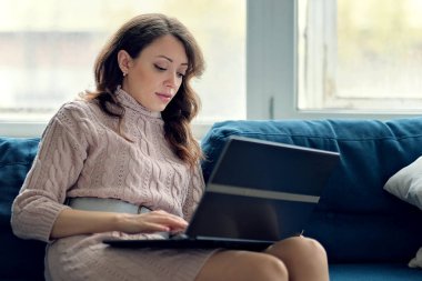 Dinlenme odasındaki kanepede dizüstü bilgisayarıyla oturan gülümseyen kadın.