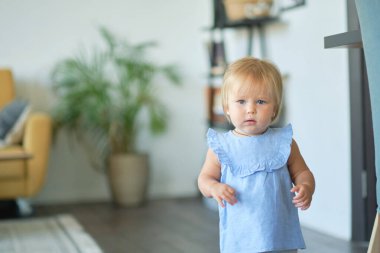 Mavi elbiseli güzel bir kızın portresi. Oturma odasında tatlı sarışın bebek