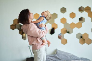 Genç anne çocuğunu kucağında tutuyor. Mutlu ve sevgi dolu bir aile. Anne yatak odasında bebeğiyle oynuyor. Anne gülen çocukla oynuyor. Aile evde.