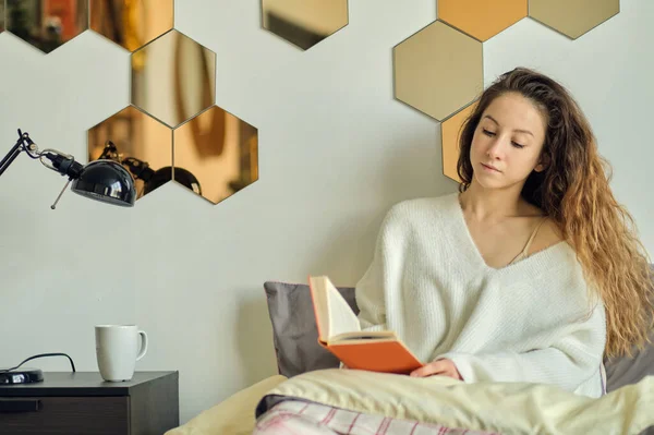 Piękna młoda kobieta w ciepłym swetrze czyta książkę. leniwy weekend w zimowy poranek. — Zdjęcie stockowe
