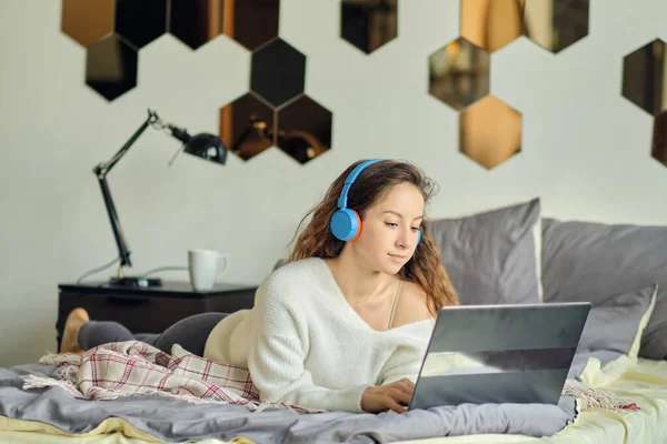 Lány fülhallgatóval hallgatja a zenét egy laptopon az ágyon otthon. — Stock Fotó