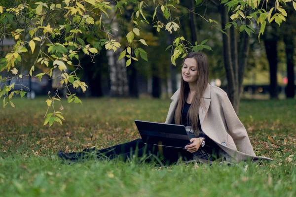 Jovem trabalha para um laptop no parque. o estudante está se preparando para exames — Fotografia de Stock