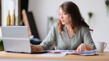 Merkez ofisten çalışan genç bir kadın. Bilgisayarı ve interneti kullanan serbest çalışan. Oturma odasındaki işyerinde. Görüntüyü kapat