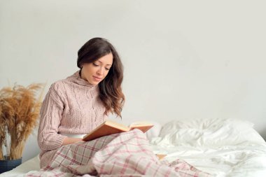 Dinlenme, rahatlama, rahatlama ve insan konsepti. Mutlu genç bir kadın yatak odasında kitap okuyor.