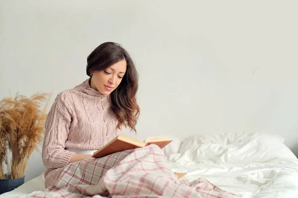 휴식, 안락, 여가 및 사람들의 개념 - 행복 한 젊은 여자가 거실에서 침대에서 책을 읽고 — 스톡 사진