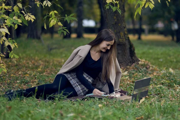 Jovem trabalha para um laptop no parque. o estudante está se preparando para exames — Fotografia de Stock