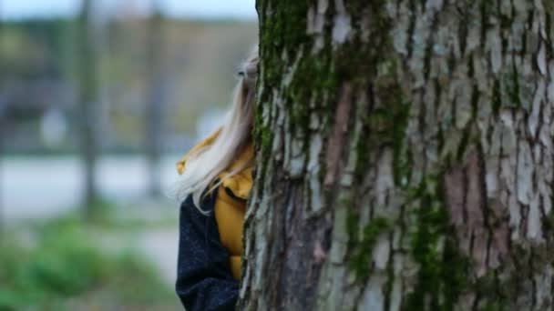 Portrait of a cute little girl. funny girl looks out from behind a tree. playing hide and seek with mom. close up Shot video. Slow motion footage — Stock Video