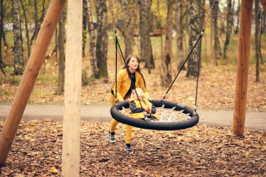 Genç kadın küçük kızını salıncakta sallıyor. Anne ve kızı birlikte eğleniyorlar. sonbahar modası