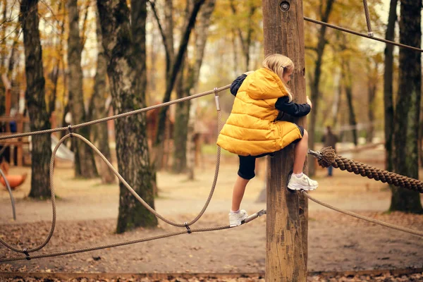 Красивая маленькая девочка лазает по веревочному парку. спортивная современная храбрая девушка. осень мода — стоковое фото