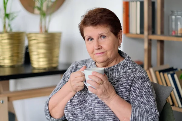 Relajada mujer mayor bebiendo café en casa en la sala de estar —  Fotos de Stock