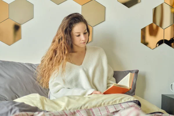 Piękna młoda kobieta w ciepłym swetrze czyta książkę. leniwy weekend w zimowy poranek. — Zdjęcie stockowe