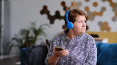 Kulaklıkla telefondan ses kaydını dinleyen kıdemli bir kadın. Görüntüyü kapat.