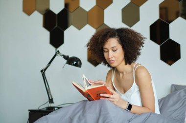 Genç siyah kadın yatakta kitap okuyor. Güzel bayan evde dinleniyor.