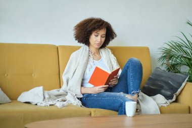 Güzel, Afro-Amerikan bir kadın kitap okuyor. Oturma odasındaki kanepede sırtüstü rahatça yatıyor. Kot pantolonuyla.