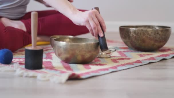 Žena hraje na tibetské pěvecké míse, zatímco sedí na podložce na jógu. Ročník tonizován. Záběry ze skladu. Zpomalené video. Zavřít — Stock video